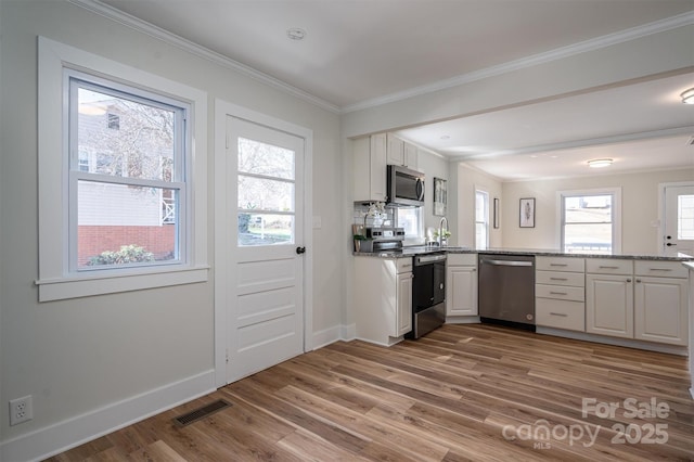 kitchen with stainless steel appliances, visible vents, ornamental molding, white cabinetry, and wood finished floors