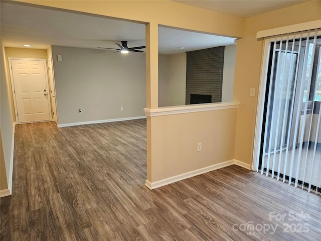 spare room featuring ceiling fan, wood-type flooring, and a brick fireplace