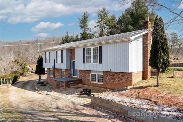 raised ranch with an outdoor fire pit, brick siding, driveway, and a chimney