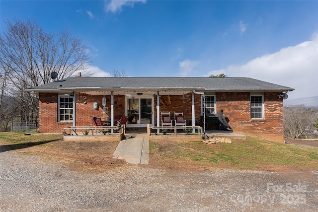 ranch-style house featuring covered porch, brick siding, a patio, and roof with shingles