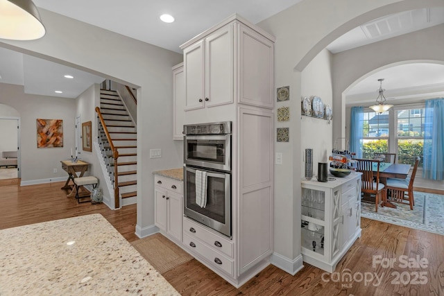 kitchen with light wood finished floors, recessed lighting, double oven, and arched walkways