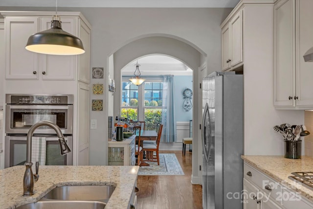 kitchen featuring a sink, wood finished floors, arched walkways, appliances with stainless steel finishes, and light stone countertops