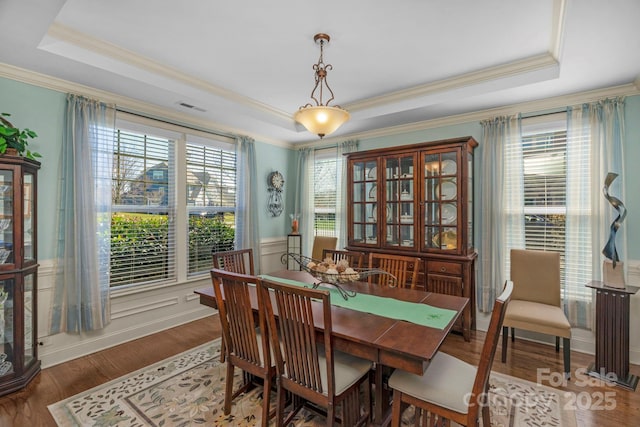 dining area featuring visible vents, a tray ceiling, wood finished floors, wainscoting, and crown molding