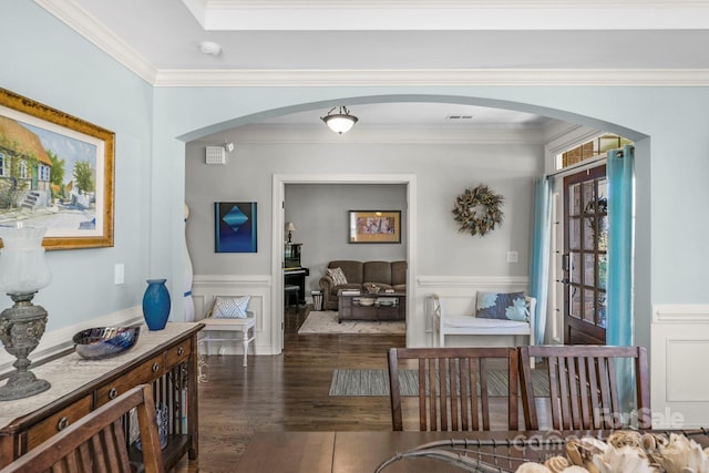 dining room with wood finished floors, arched walkways, ornamental molding, wainscoting, and a decorative wall