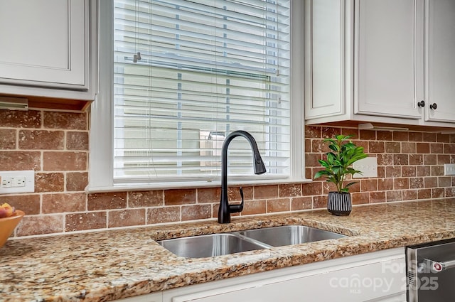 kitchen featuring stainless steel dishwasher, white cabinetry, light stone counters, and a sink