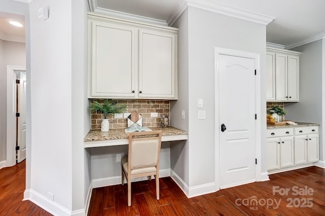 interior space featuring baseboards, ornamental molding, built in desk, dark wood finished floors, and tasteful backsplash