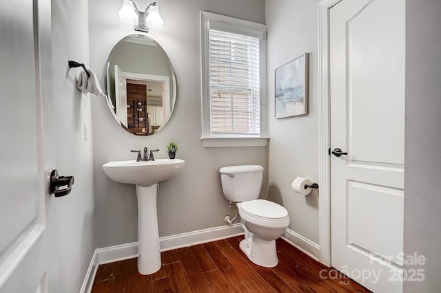 half bathroom featuring a sink, toilet, baseboards, and wood finished floors