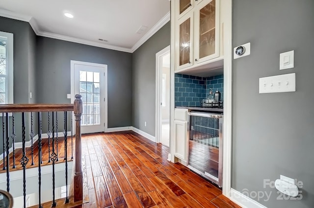 entryway featuring beverage cooler, wood finished floors, baseboards, ornamental molding, and a bar