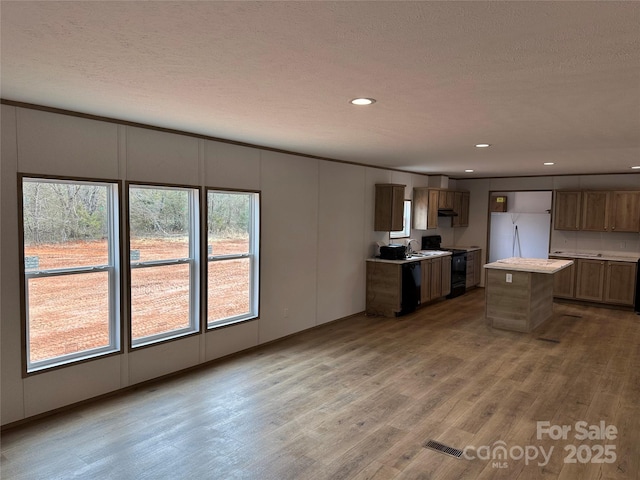 kitchen with sink, a center island, a textured ceiling, light hardwood / wood-style floors, and black appliances