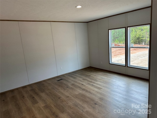 spare room featuring ornamental molding, hardwood / wood-style floors, and a textured ceiling