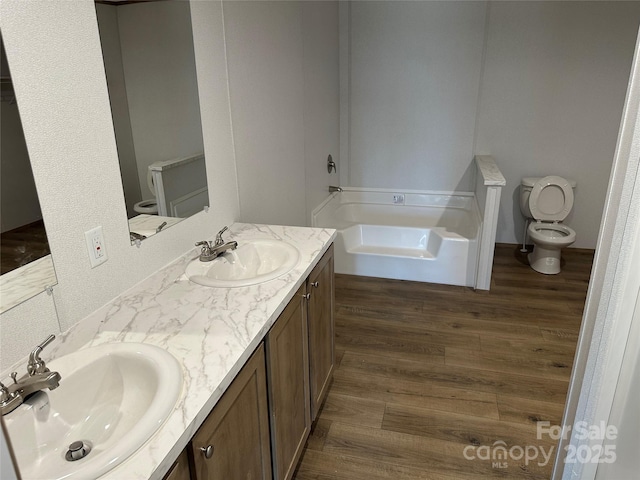 bathroom featuring vanity, a tub to relax in, wood-type flooring, and toilet