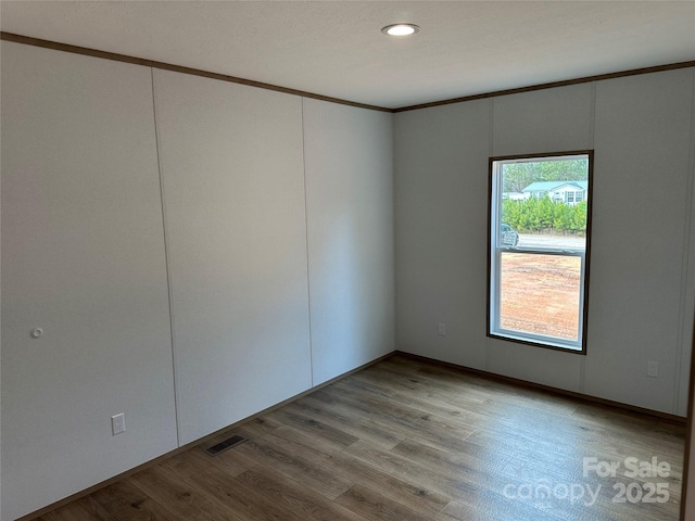 spare room featuring crown molding and light hardwood / wood-style floors