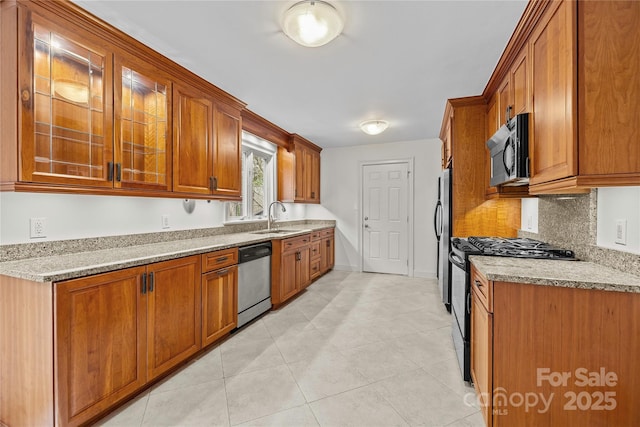 kitchen with sink, light tile patterned floors, appliances with stainless steel finishes, light stone countertops, and decorative backsplash