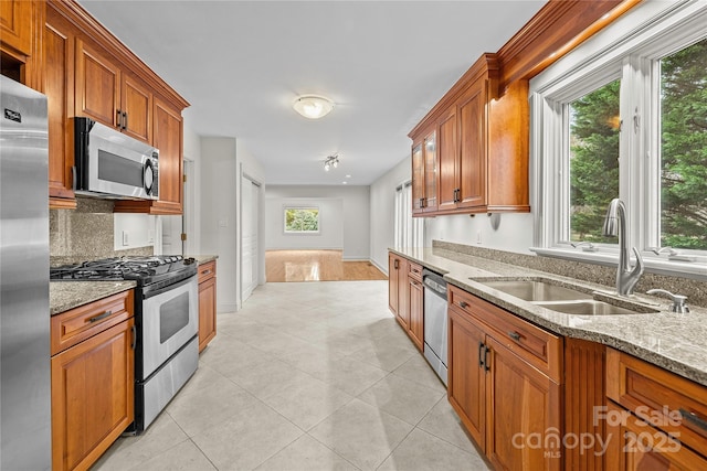 kitchen featuring sink, decorative backsplash, light tile patterned floors, light stone counters, and stainless steel appliances