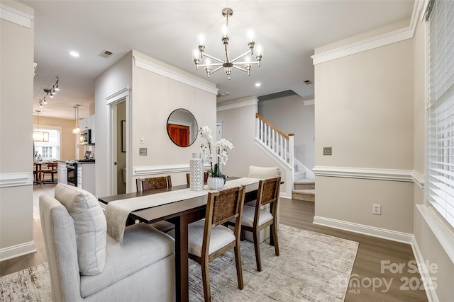 dining space featuring ornamental molding, wood-type flooring, rail lighting, and a notable chandelier