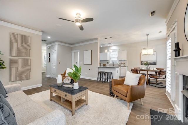 living room with ornamental molding, sink, ceiling fan, and light wood-type flooring