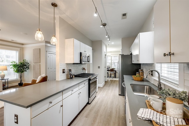 kitchen with appliances with stainless steel finishes, pendant lighting, sink, white cabinets, and light hardwood / wood-style floors