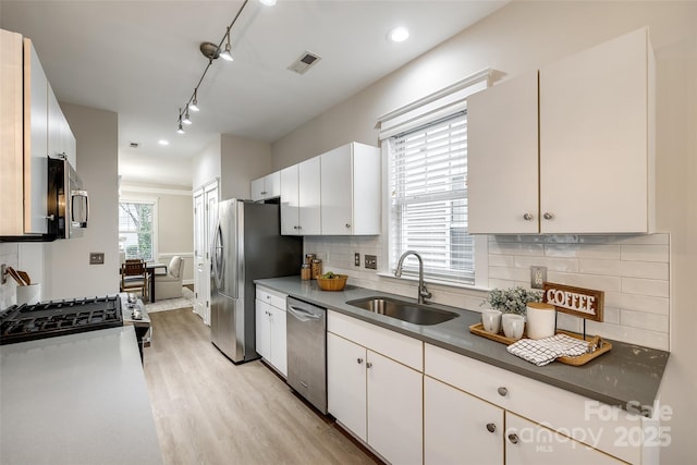 kitchen featuring sink, light wood-type flooring, white cabinets, stainless steel appliances, and backsplash