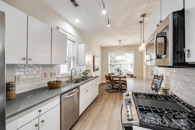 kitchen featuring sink, light hardwood / wood-style flooring, pendant lighting, stainless steel appliances, and white cabinets