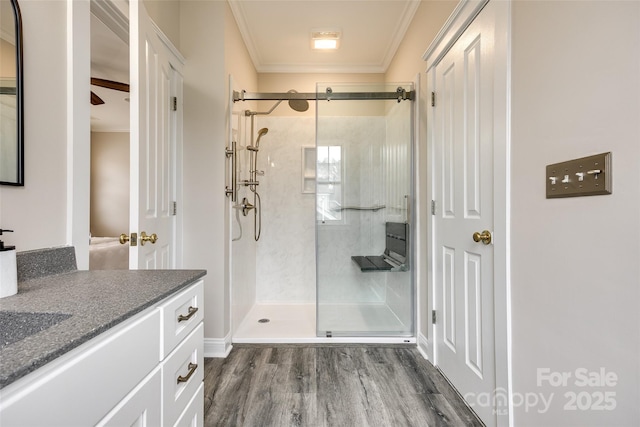 bathroom with wood-type flooring, ornamental molding, vanity, ceiling fan, and a shower with door