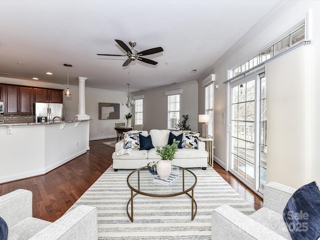 living room with ceiling fan with notable chandelier, crown molding, decorative columns, and dark hardwood / wood-style floors