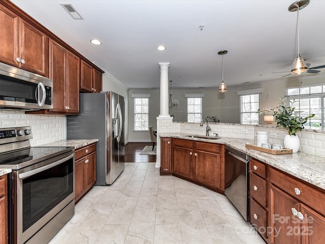 kitchen with stainless steel appliances, decorative light fixtures, sink, ornate columns, and light stone counters