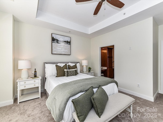 bedroom with a tray ceiling, light carpet, ensuite bathroom, and ceiling fan