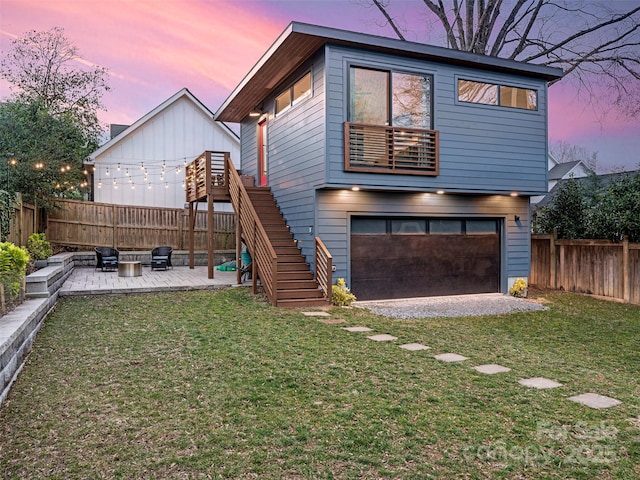 back house at dusk with a patio, a garage, a wooden deck, and a yard