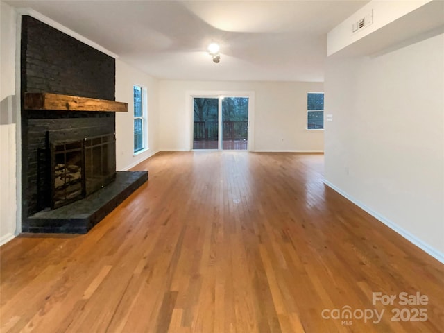 unfurnished living room with a large fireplace, wood finished floors, visible vents, and baseboards