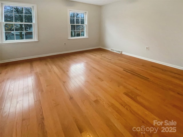 empty room featuring light wood finished floors, visible vents, and baseboards