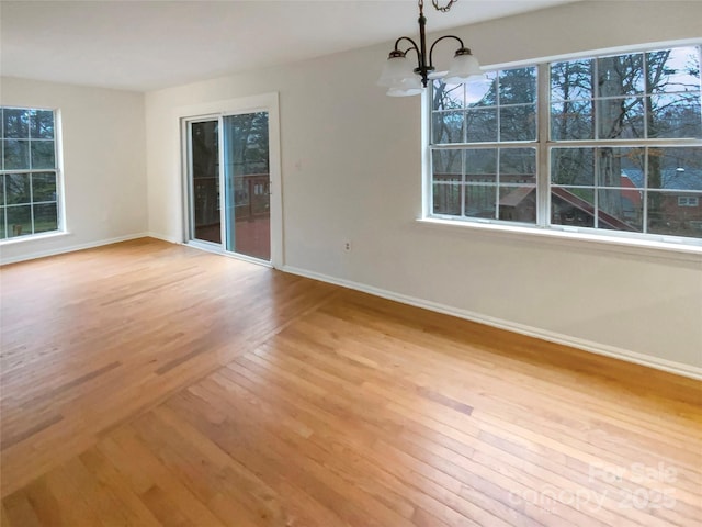 spare room featuring plenty of natural light, light wood-type flooring, an inviting chandelier, and baseboards