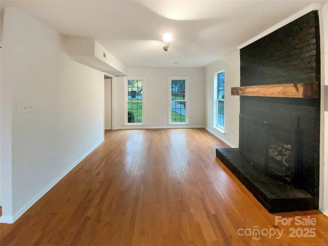 unfurnished living room with a brick fireplace, wood finished floors, and baseboards