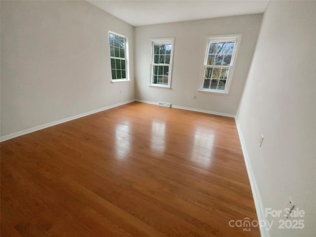 empty room featuring a wealth of natural light, light wood-type flooring, visible vents, and baseboards