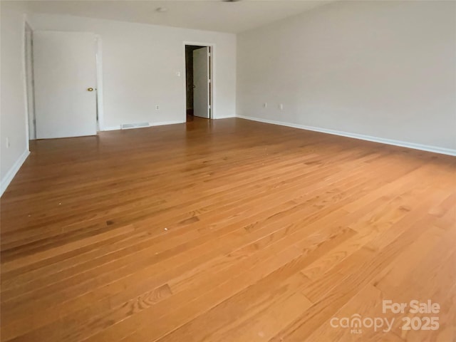 spare room featuring wood finished floors, visible vents, and baseboards