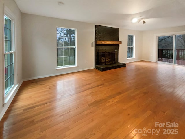 unfurnished living room with a brick fireplace, light wood-style flooring, and baseboards