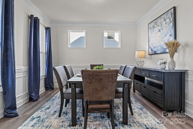dining room with wood finished floors, a decorative wall, ornamental molding, and a wainscoted wall