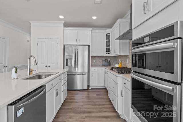 kitchen with ornamental molding, light countertops, white cabinets, stainless steel appliances, and a sink