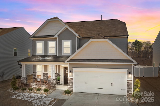 craftsman-style house featuring fence, stone siding, covered porch, and driveway