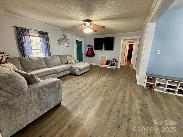 living room with ornamental molding, ceiling fan, a textured ceiling, wood finished floors, and baseboards