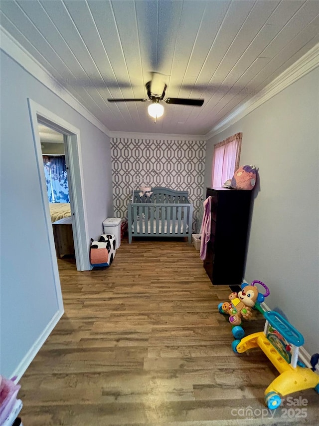 bedroom with an accent wall, ornamental molding, wood finished floors, and baseboards