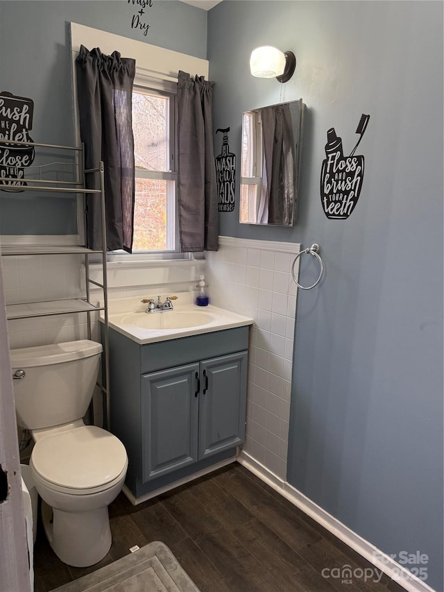 half bath featuring tile walls, toilet, wainscoting, vanity, and wood finished floors