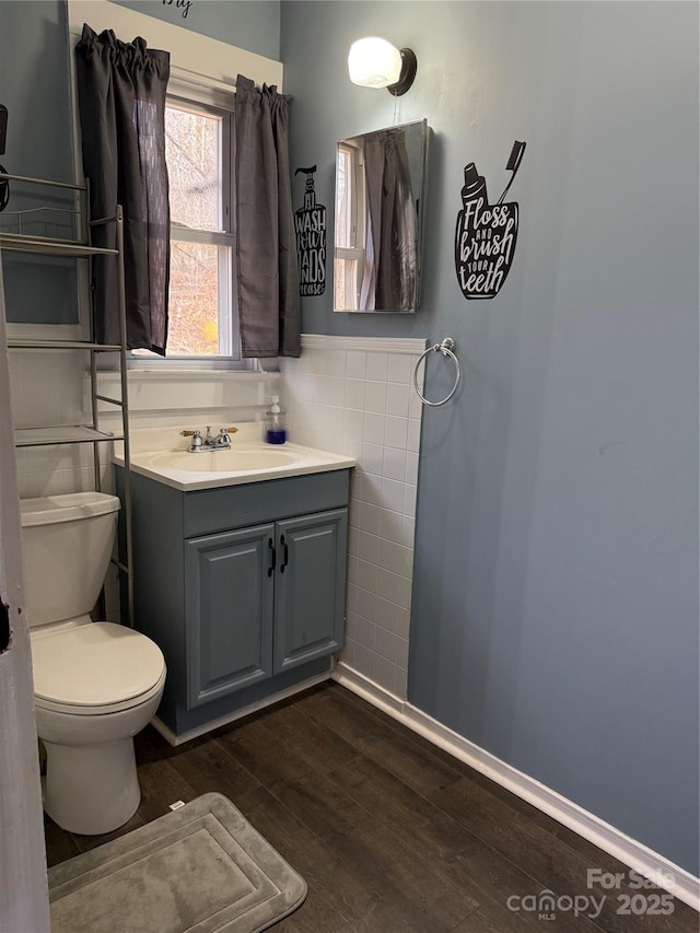 half bathroom featuring toilet, wood finished floors, vanity, tile walls, and wainscoting