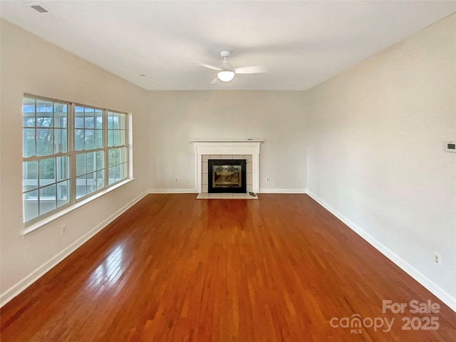 unfurnished living room featuring dark wood-style floors, baseboards, ceiling fan, and a tiled fireplace