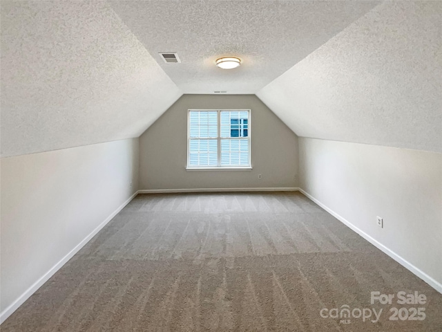 bonus room with lofted ceiling, a textured ceiling, carpet flooring, visible vents, and baseboards