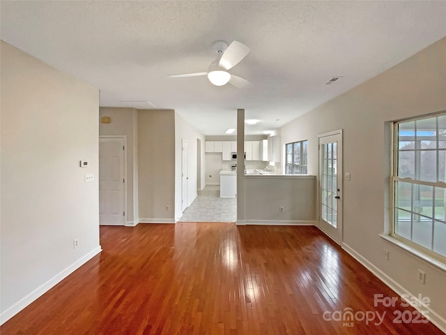 unfurnished living room featuring a ceiling fan, plenty of natural light, baseboards, and wood finished floors