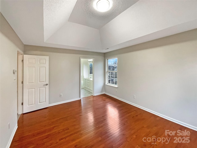 unfurnished bedroom with a textured ceiling, a tray ceiling, wood finished floors, and baseboards