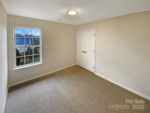 unfurnished bedroom with carpet, a closet, a textured ceiling, and baseboards