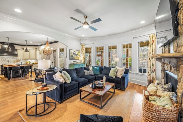 living room featuring light wood-type flooring, ceiling fan, ornamental molding, and a fireplace