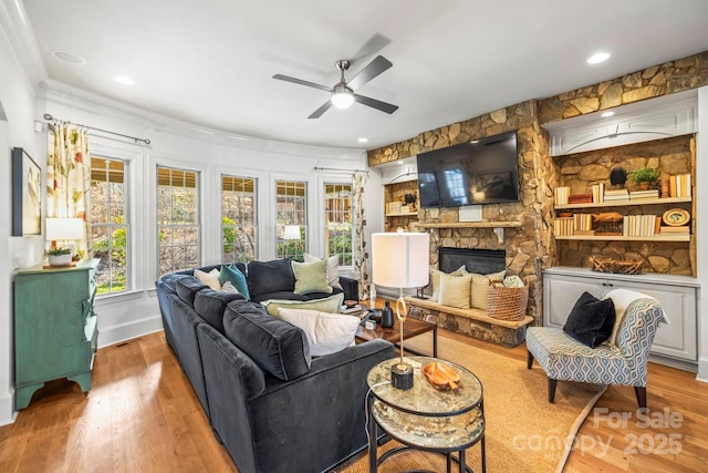 living room featuring ceiling fan, hardwood / wood-style flooring, and a stone fireplace