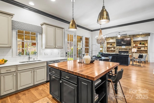 kitchen with hanging light fixtures, butcher block counters, light wood-type flooring, a center island, and sink